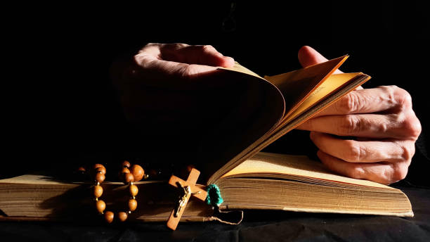 Hands flipping Bible in dark. Book, cross, rosary on black background. stock photo