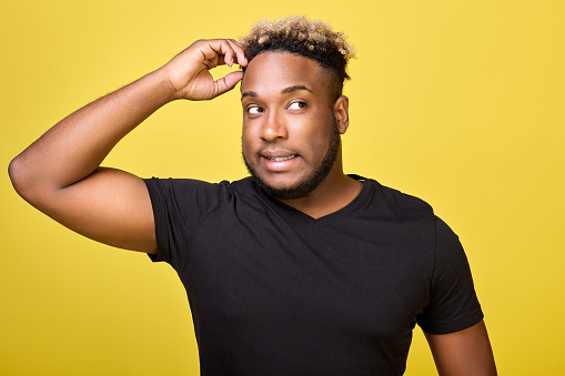 Brutal guy in casual clothes looks tense and nervously scratches his head with his hand looking to the side. A puzzled dark-skinned man looks excitedly to the side on a yellow background