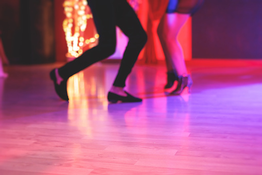 Dancing shoes of a couple, couples dancing traditional latin argentinian dance milonga in the ballroom, tango salsa bachata kizomba lesson, festival on a wooden floor, red, purple and violet lights