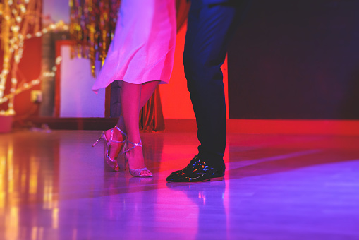 Dancing shoes of a couple, couples dancing traditional latin argentinian dance milonga in the ballroom, tango salsa bachata kizomba lesson, festival on a wooden floor, red, purple and violet lights