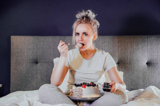 istock Emotionally stressed, shocked woman eating cake and holding a remote control while watching TV in bed. Scary horror movie or terrible news, scare in her eyes Overeating, Jamming of negative emotions 1456806043