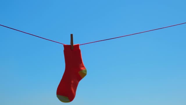 on rope against blue sky hangs one forgotten lost orange sock.concept of household chores.soft focus