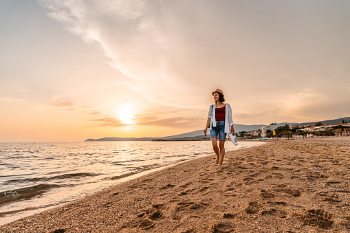 Beautiful young woman walking on the beach in Thasos, Greece as the sun sets.