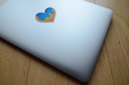 A closed grey laptop with a heart shape Ukrainian flag sticker on it, against a wooden background
