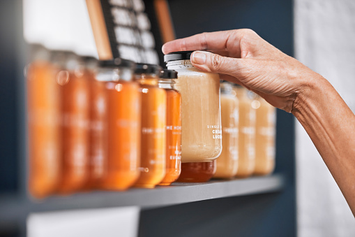 Hands, jar and honey shelf for inventory check, product pricing or labeling in organic retail store. Hand in small business, management or market advertising of healthy glass food products for sale