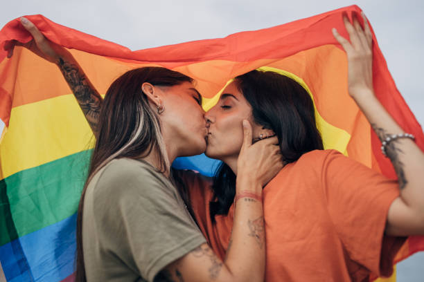 Happy couple kissing Two women, lesbian couple holding a rainbow flag and kissing outdoors gay long hair stock pictures, royalty-free photos & images