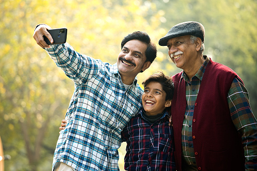 Three generations of males taking selfie using mobile phone at park