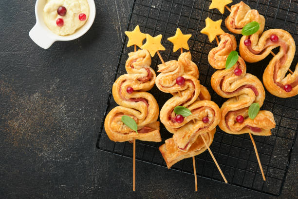 Christmas or New Year appetizer. Christmas tree shape puff pastry buns with cheese and ham. Group of Christmas tree shapes on wooden board. Festive idea for Christmas or New Year dinner. Top view. Christmas or New Year appetizer. Christmas tree shape puff pastry buns with cheese and ham. Group of Christmas tree shapes on wooden board. Festive idea for Christmas or New Year dinner. Top view. twisted bacon stock pictures, royalty-free photos & images