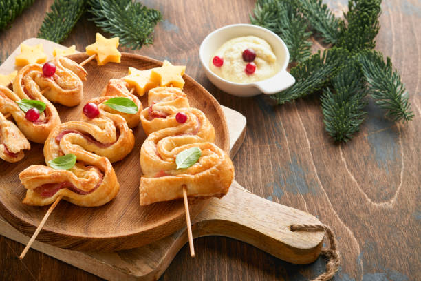 istock Christmas or New Year appetizer. Christmas tree shape puff pastry buns with cheese and ham. Group of Christmas tree shapes on wooden board. Festive idea for Christmas or New Year dinner. Top view. 1456817696