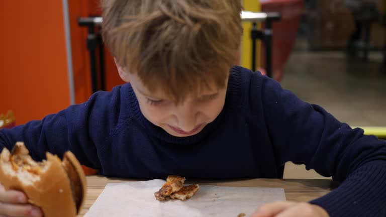 Boy child eating portrait does not like a burger in fast food restaurant spit it out on a table