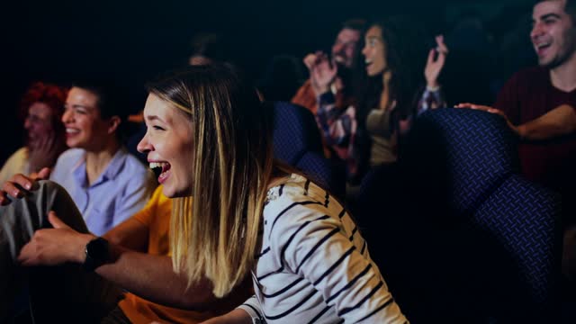 Group of cheerful people laughing while watching movie in cinema.