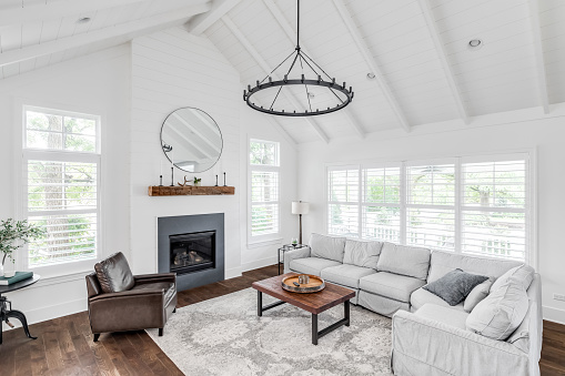A modern farmhouse living room with shiplap, exposed white beams, a fireplace, and furniture on hardwood floors.