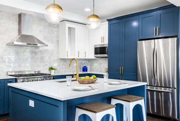 A blue kitchen with stainless steel appliances. A luxurious white and blue kitchen with gold hardware, stainless steel appliances, and white marbled granite counter tops. cupboard stock pictures, royalty-free photos & images