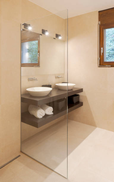 istock Modern bathroom front view with large light marble slabs. There are two sinks with a large mirror illuminated by spotlights 1456823175