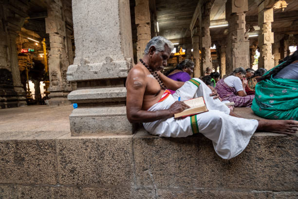 un anziano sacerdote del tempio indù in abiti tradizionali legge un libro - casita foto e immagini stock