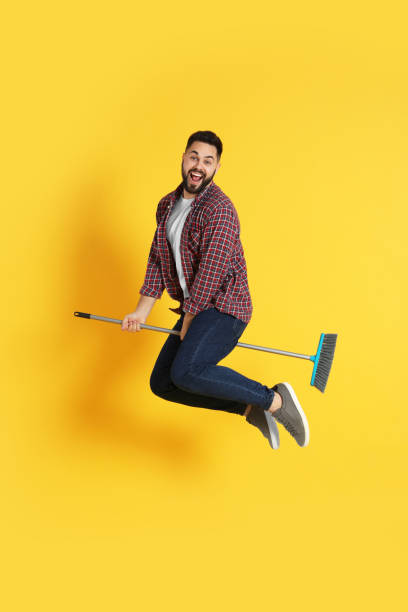 istock Young man with broom jumping on orange background 1456825062