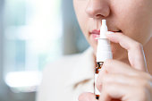 Close-up shot of sick young woman using nasal spray