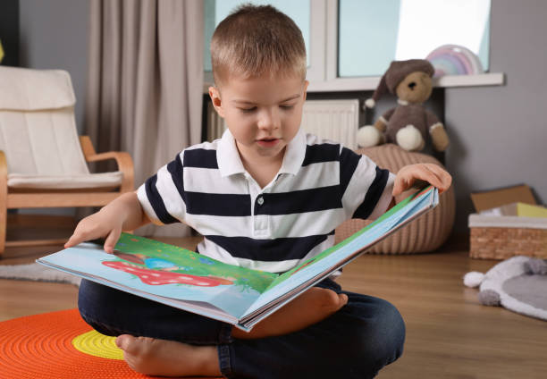 istock Cute little boy reading book on floor at home 1456826164