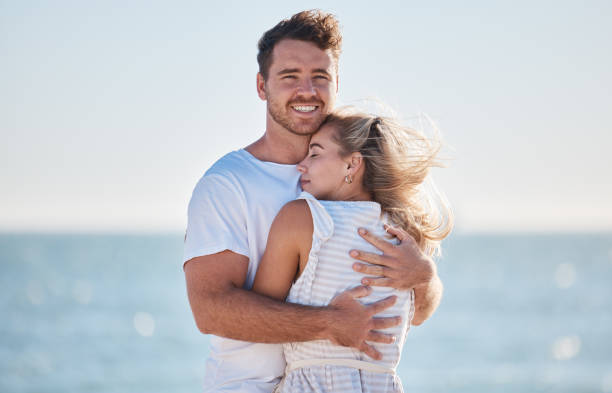 istock Hug, love and couple at the beach for a date, travel and summer commitment together. Affection, happy and portrait of a man and woman hugging for comfort, happiness and marriage at the ocean 1456827424