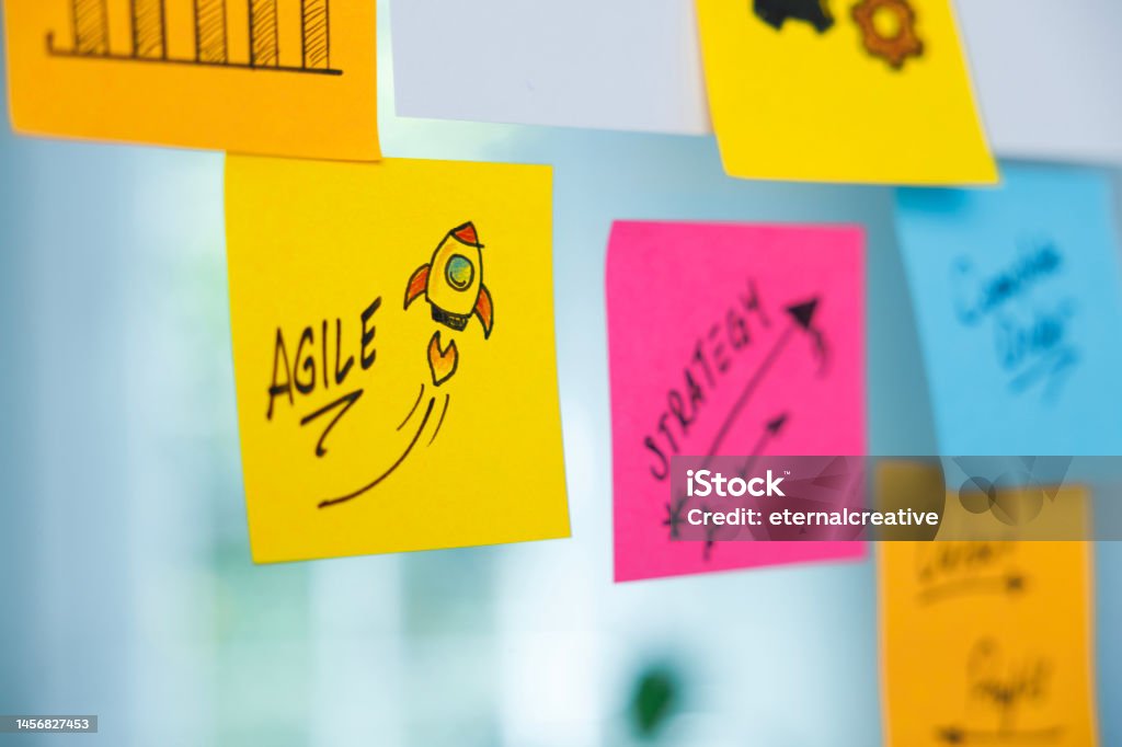 The word Agile and rocket symbol on a yellow adhesive note Workflow planning in office glass. Colored adhesive note papers and the word Agile and rocket symbol Agility Stock Photo