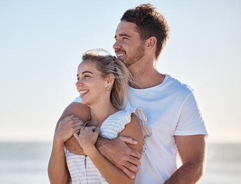Happy couple, love and beach vacation in summer with a hug, care and support while thinking about future and marriage. Man and woman outdoor by the ocean for fresh air, travel and holiday in nature