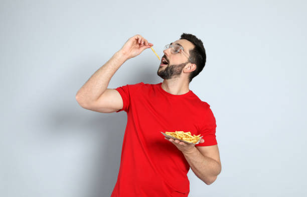 istock Man eating French fries on grey background 1456829049