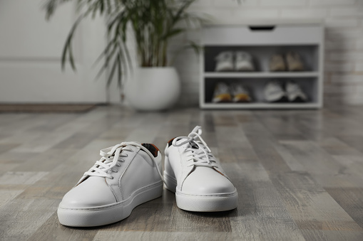 Pair of stylish white sneakers on floor in hallway, space for text