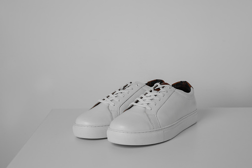 Pair of stylish sneakers on white table against light background. Space for text