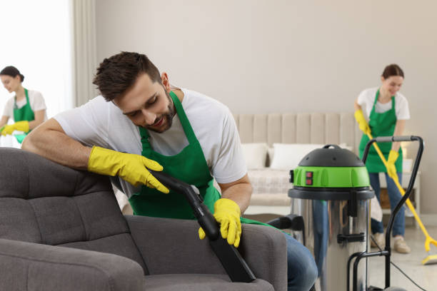 istock Professional janitor in uniform vacuuming armchair indoors 1456829545