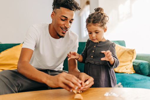 Happy father and daughter opening a fortune cookie at home. Playful single father having fun with his daughter in the living room. Dad and daughter spending some quality time together.