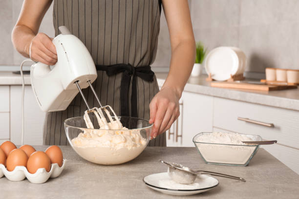 istock Woman whipping white cream with mixer at light grey table in kitchen, closeup 1456831083