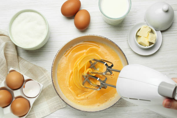istock Woman beating eggs with mixer at white wooden table, top view 1456831493