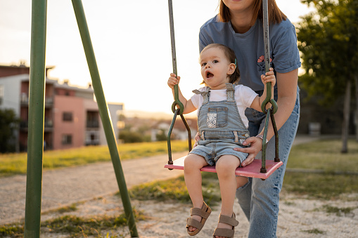 small little girl toddler with her mother in park woman help her child to swing while having fun outdoor in sunny day leisure family growing up concept copy space real people