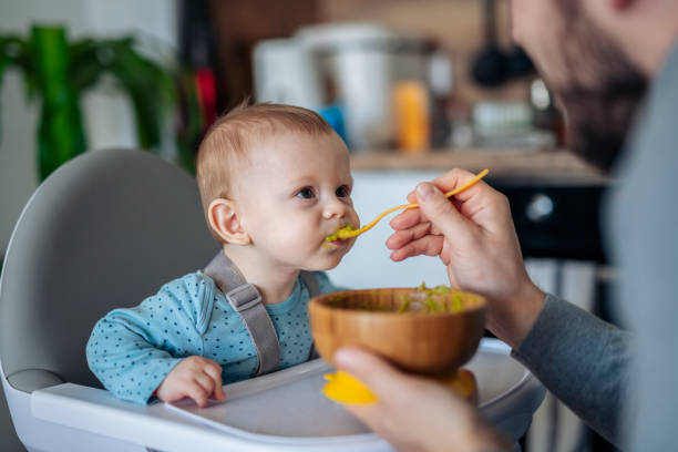 Caring single father spoon feeding his beautiful son. Caring single father spoon feeding his beautiful son at home. high chair stock pictures, royalty-free photos & images