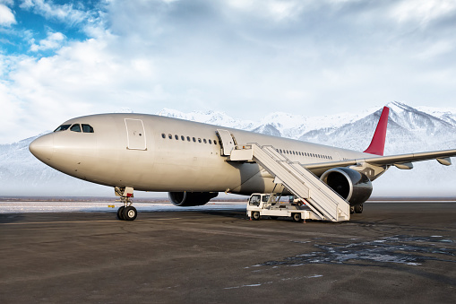 Avión de pasajeros de fuselaje ancho con escalones de embarque en la plataforma del aeropuerto en el fondo de altas y pintorescas montañas cubiertas de nieve photo