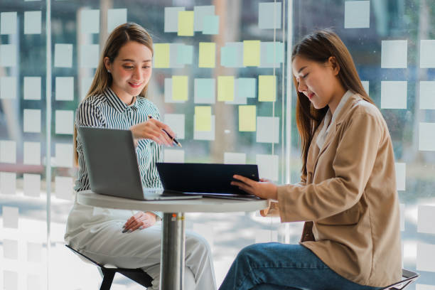 Attractive and happy Asian businesswoman showing something on tablet screen Share her creative marketing ideas with brainstorming colleagues in the office. stock photo