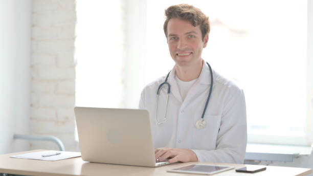istock Young Doctor Smiling at Camera While sitting in Clinic 1456843288