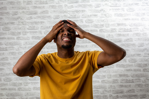 Handsome African young man wearing casual yellow t-shirt suffering from headache desperate and stressed because pain and migraine. hands on head. Negative human emotions and feelings concept