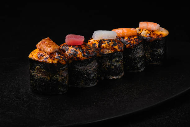 istock Baked sushi roll with different kind of fish on their top on black background 1456847255