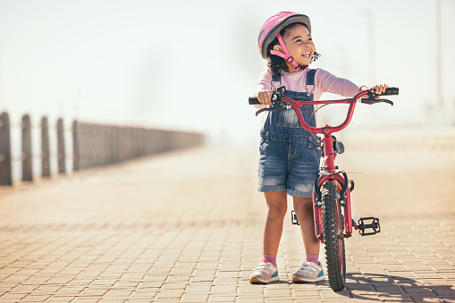 Fun, thinking and girl cycling with a bike in the city for sustainability, carbon footprint and eco friendly transport. Happy, smile and child with an idea and a bicycle in the street for happiness