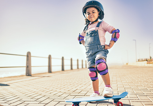 Skateboard, cool and girl with power in the city while riding during summer. Action, urban and portrait of a strong young child learning, playing and skateboarding in the street for happiness