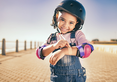 Happy, arm first aid or girl child with bandage for bruise from skating, cycling or accident in street. Portrait, smile or kid with helmet for motivation, wellness health fun at beach, sea or ocean