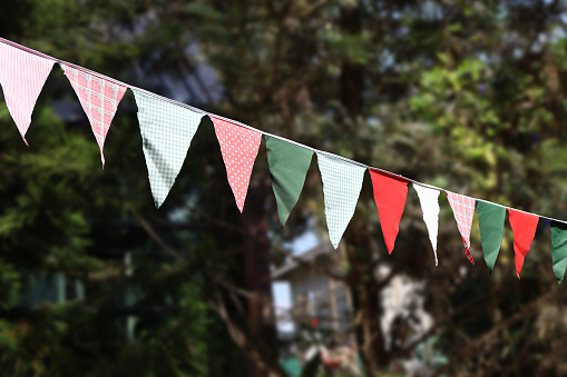 Festive ribbon of multicolored triangle flags on the white clouds and blue sky background. Celebration party, holiday fair, festival decorations.