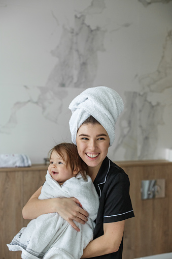 Mom and baby look in mirror and smile in bathroom. White towels. Cozy house. Family time.