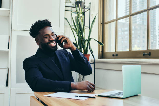 istock African American man smiling while multitasking at desk, talking on mobile phone and working on laptop 1456853632
