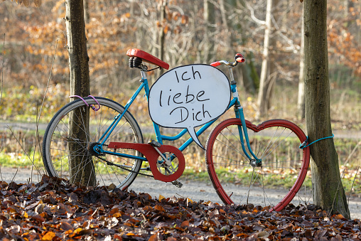 Old bicycle with heart shaped tire and a German love message on a speech balloon.