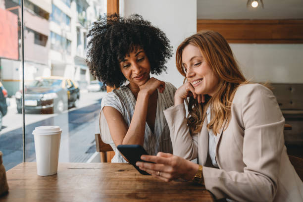 Two young adult women looking at smartphone together at the cafe stock photo