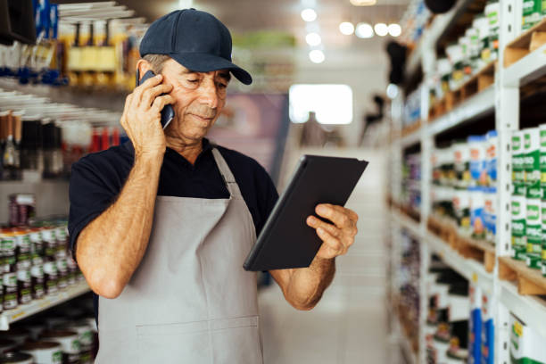 uomo anziano che lavora in un negozio di ferramenta utilizzando una tavoletta digitale mentre effettua una telefonata. concetto di piccola impresa. - senior adult aging process supermarket shopping foto e immagini stock