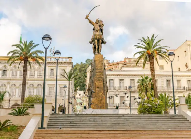 Photo of El Amir Abdelkader statue with flying pigeons and palm trees