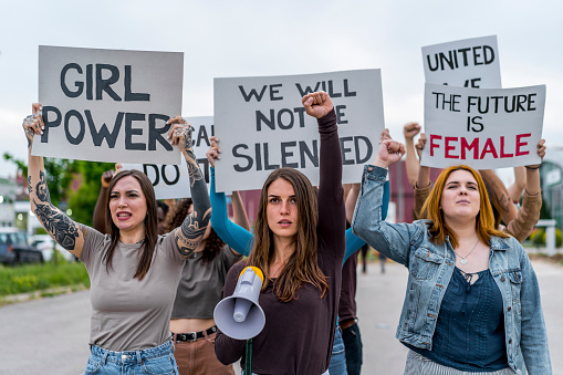 Group of young women protesting for equality and women's rights. Holding hand-made signs on cardboard and marching together in the city streets